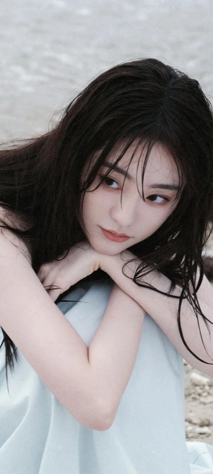 一名长发女性靠在浅蓝色背景前，双臂交叠并注视镜头。