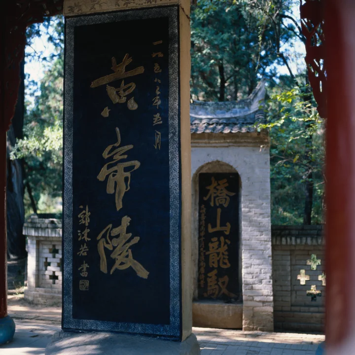 画面展示一座刻有书法的古迹门景，后方可见石墙、树木和传统瓦檐。