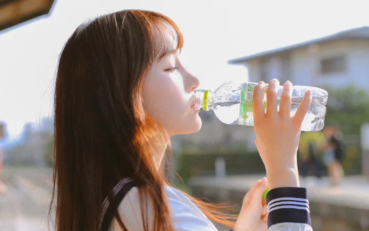 一名年轻女性在户外举着透明水瓶喝水。