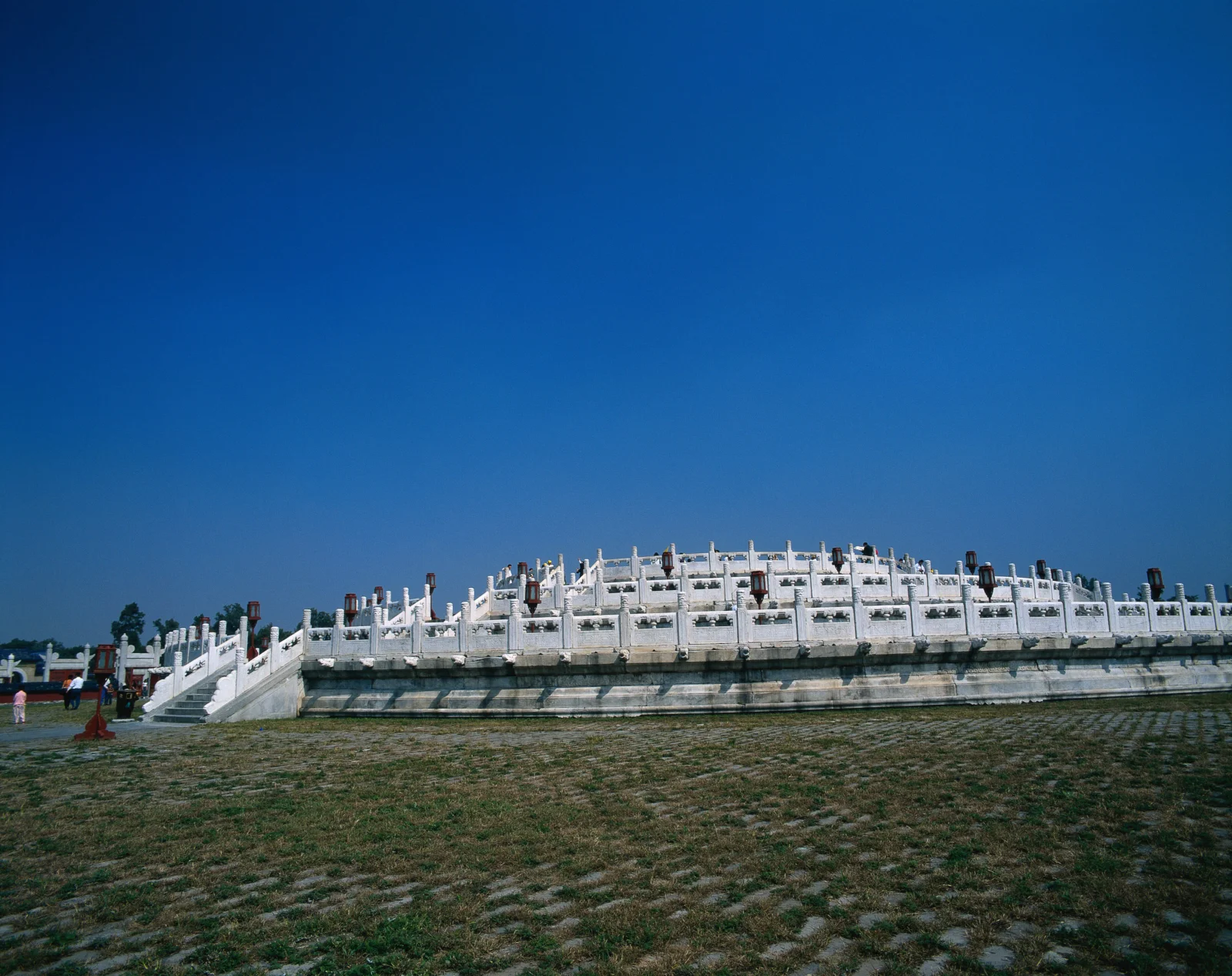 一座白色石质 ceremonial terrace stands outdoors above a grassy foreground beneath a clear blue sky.