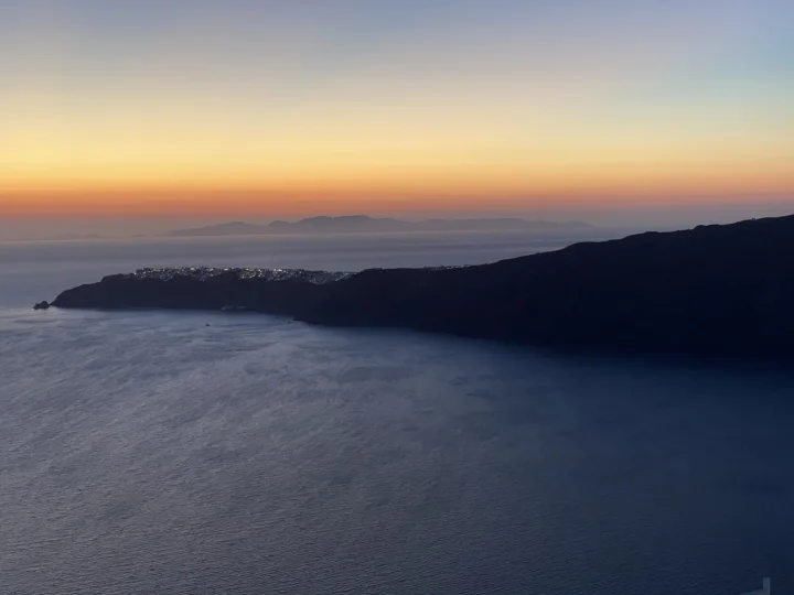 暮色中的海面与深色海岸线映衬着橙粉色的日落天空。