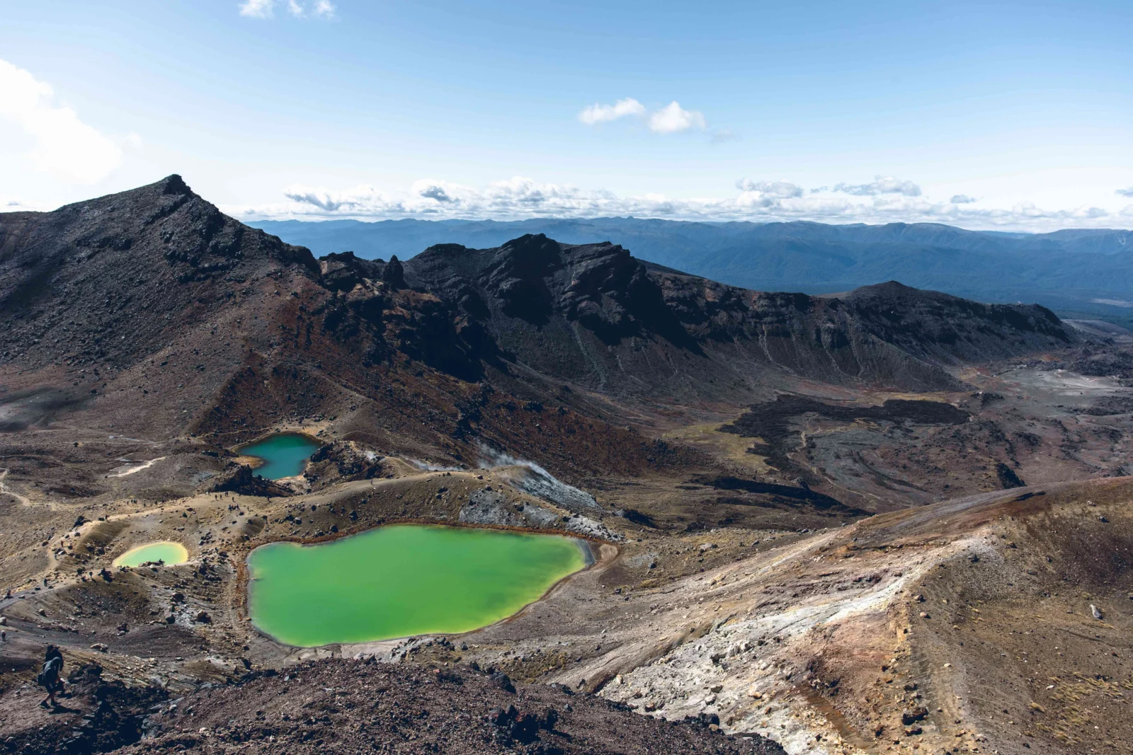 画面展示了蓝天下的火山山脉、深色岩地和几座翠绿色湖泊。