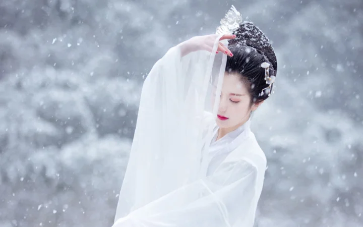 一名身穿白色衣饰的女性在飘雪背景前低头 posed。