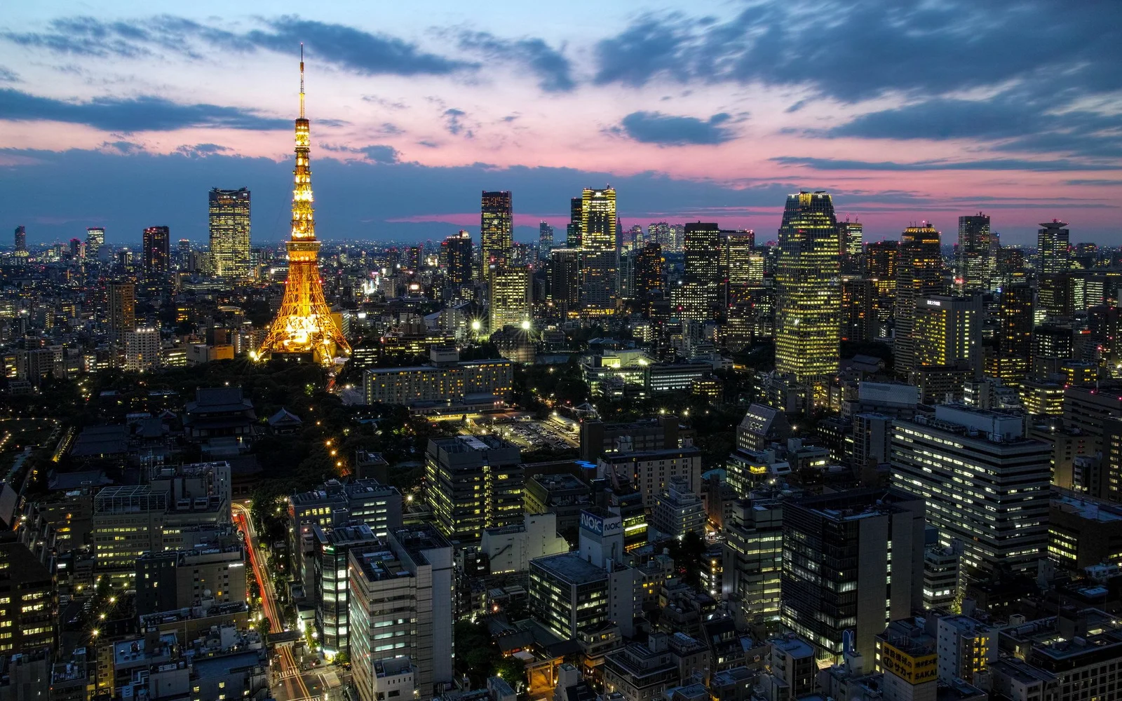 夕暮れの空の下、東京タワーが高層ビルの街並みの中で金色に輝いている。
