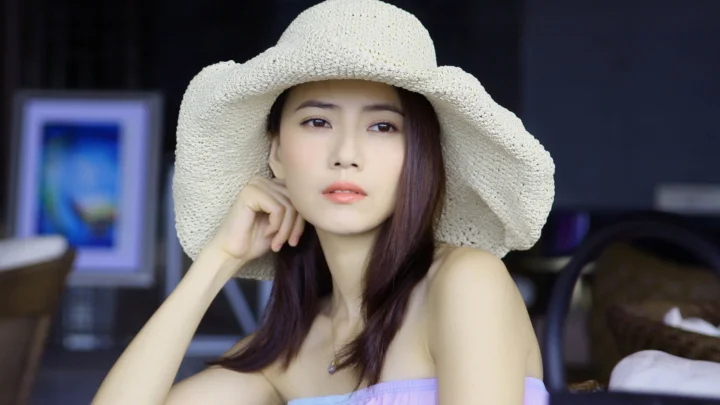 一位戴着浅色宽檐草帽的成年女性在室内面向镜头摆姿势。