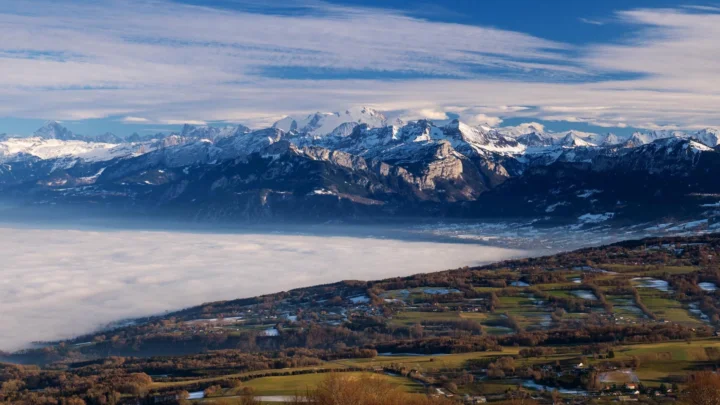 雪山、云雾笼罩的山谷与山脚下的田野组成壮阔的自然全景。