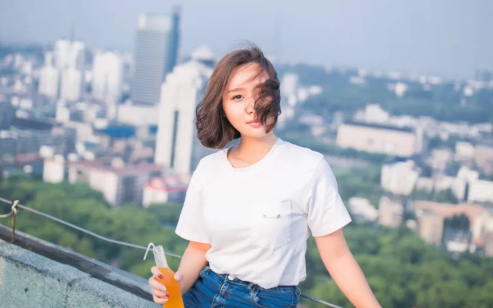 一名穿白色T恤的成年女性站在城市天际线前，微风吹拂着她的短发。