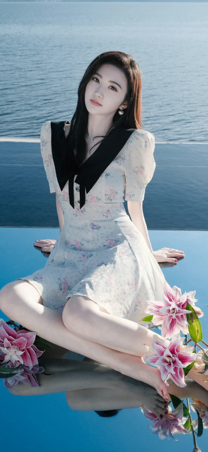 一名女子穿着浅色碎花连衣裙坐在水边，周围点缀着粉色花朵。