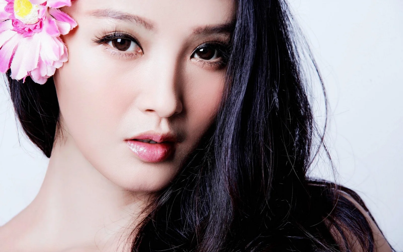 검은 머리 여성의 얼굴을 크게 담은 초상으로, 얼굴 옆에 분홍색 꽃이 장식되어 있습니다.