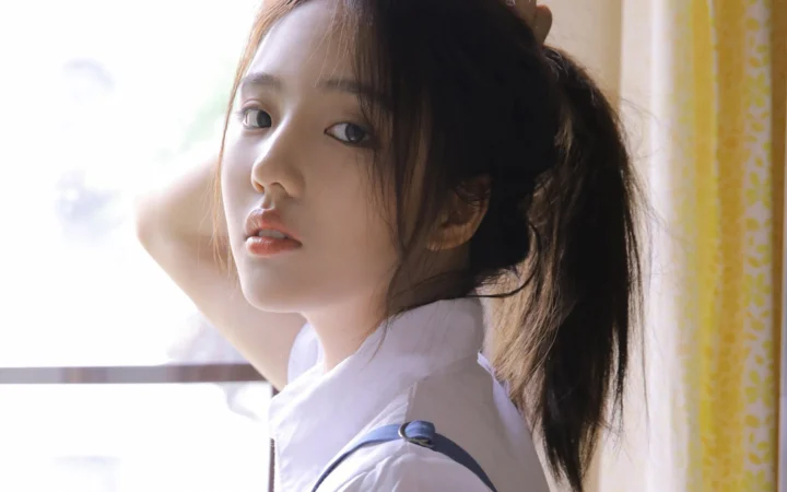 창가에서 한 여성이 카메라를 돌아보며 부드러운 자연광이 얼굴을 비추고 있다.