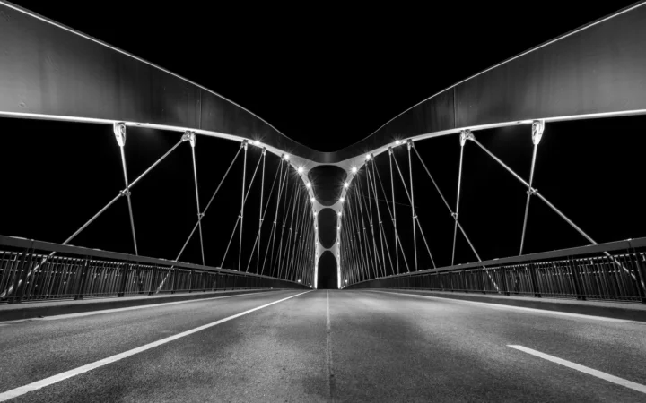 黑白画面中，一座悬索桥的道路从低视角延伸向中央拱门。