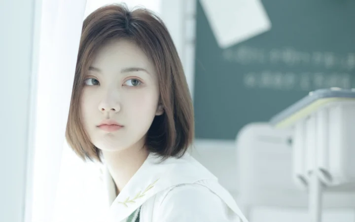 一位留着棕色短发、穿白色衣服的女性在室内望向一侧。