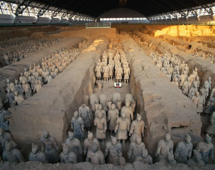 室内展馆中排列着大量兵马俑雕像，土坑与拱形屋顶共同构成壮观的考古遗址景观。