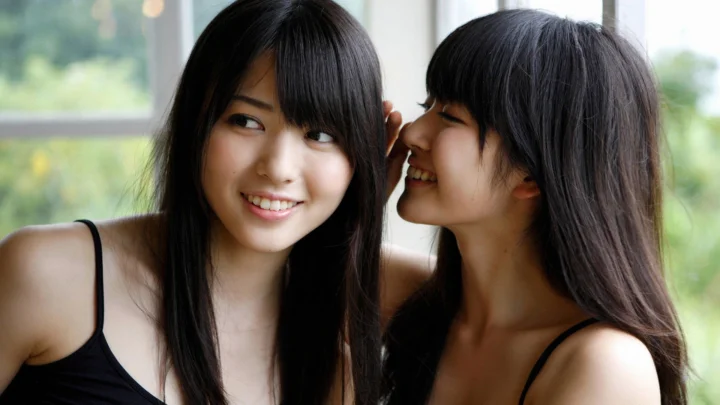 两位女性在窗边靠近彼此微笑。