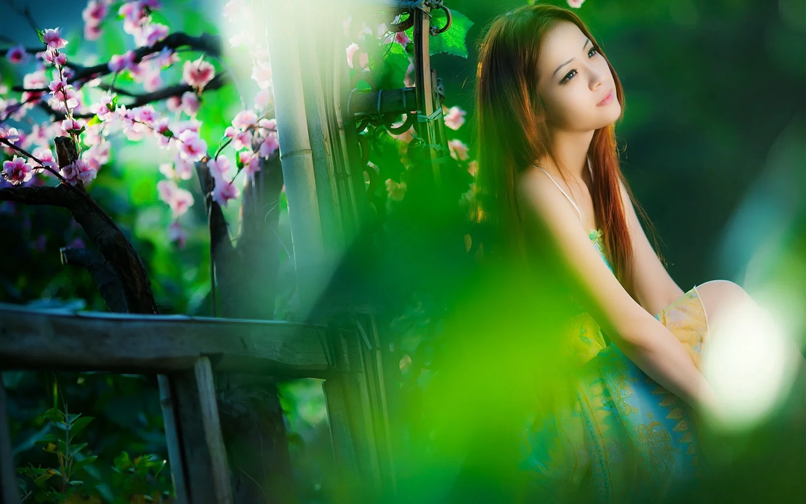 一名女子置身于樱花与竹林之间，前景的绿色植物营造出朦胧的层次感。