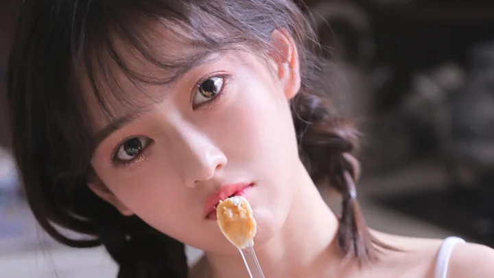 一名女性近距离看向镜头，嘴边含着一把盛有食物的勺子。