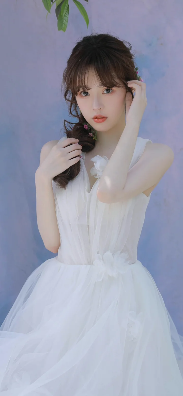 一名女子身穿白色连衣裙，在淡紫色背景前摆姿势。