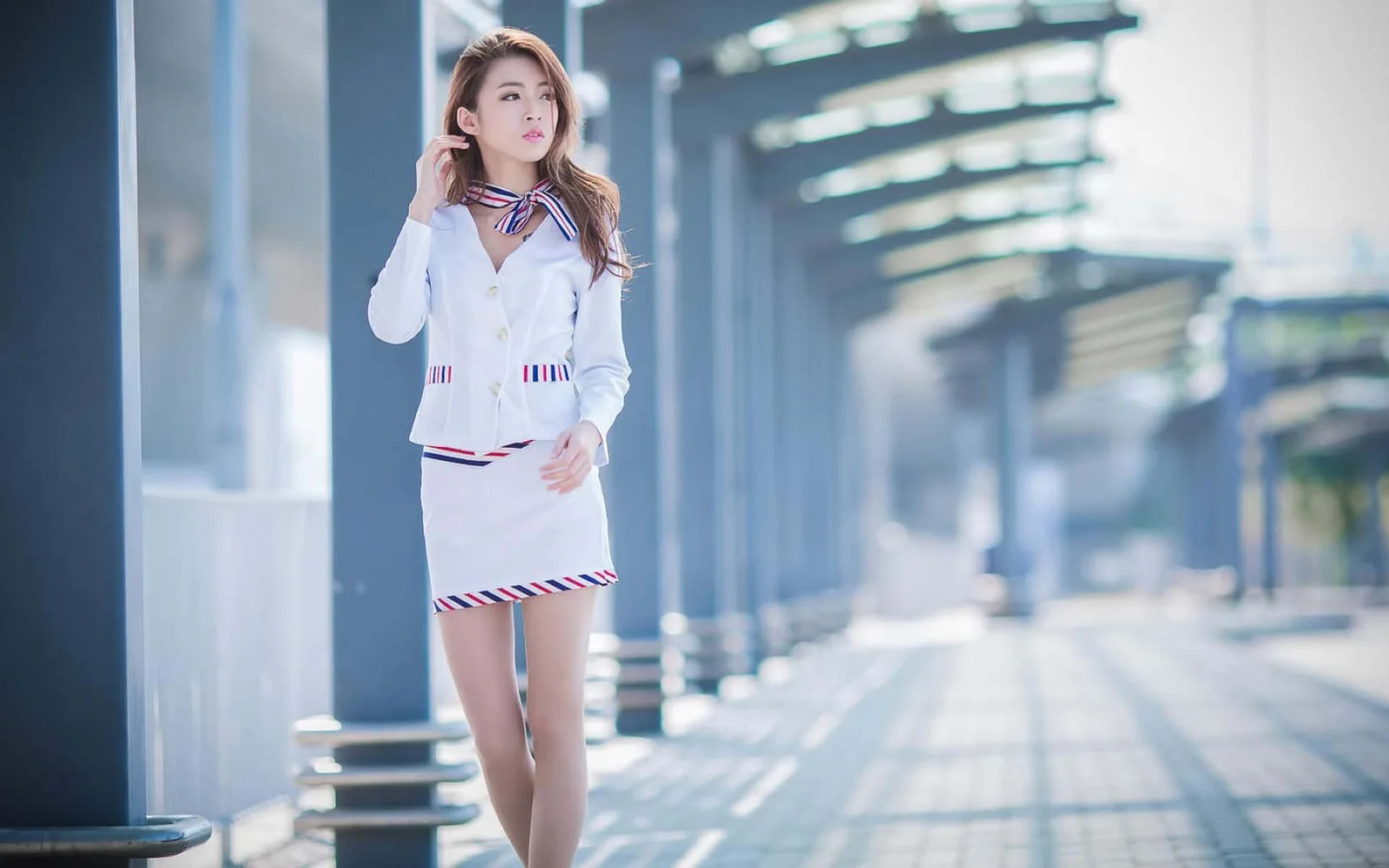 一名身穿白色職業套裝的成年女性站在現代建築旁的人行道上。