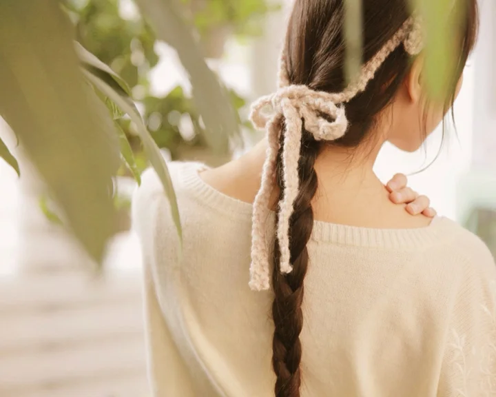 一名身穿浅色毛衣、留着长辫子的女子站在柔和光线中，侧身回望。