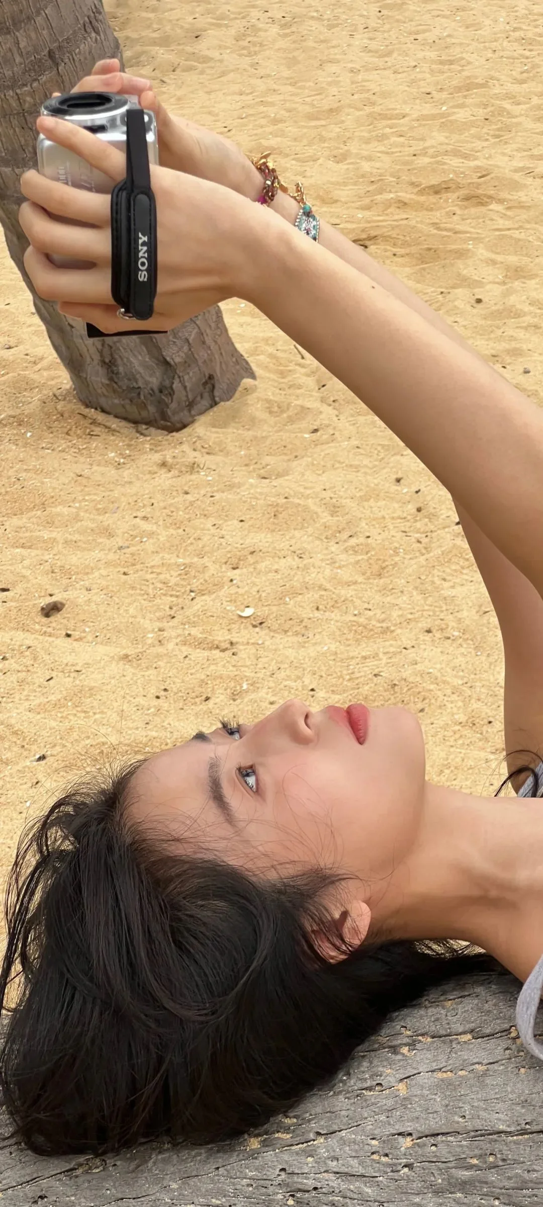 一名女子躺在沙滩上，手边放着相机。