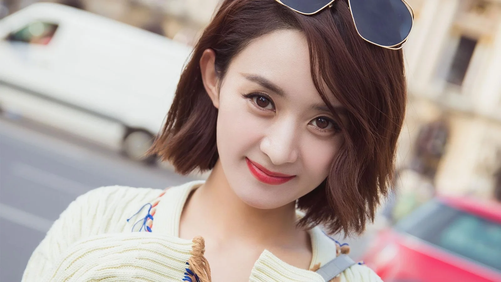선글라스를 머리에 올린 미소 짓는 여성이 거리에서 카메라를 가까이 바라보고 있습니다.