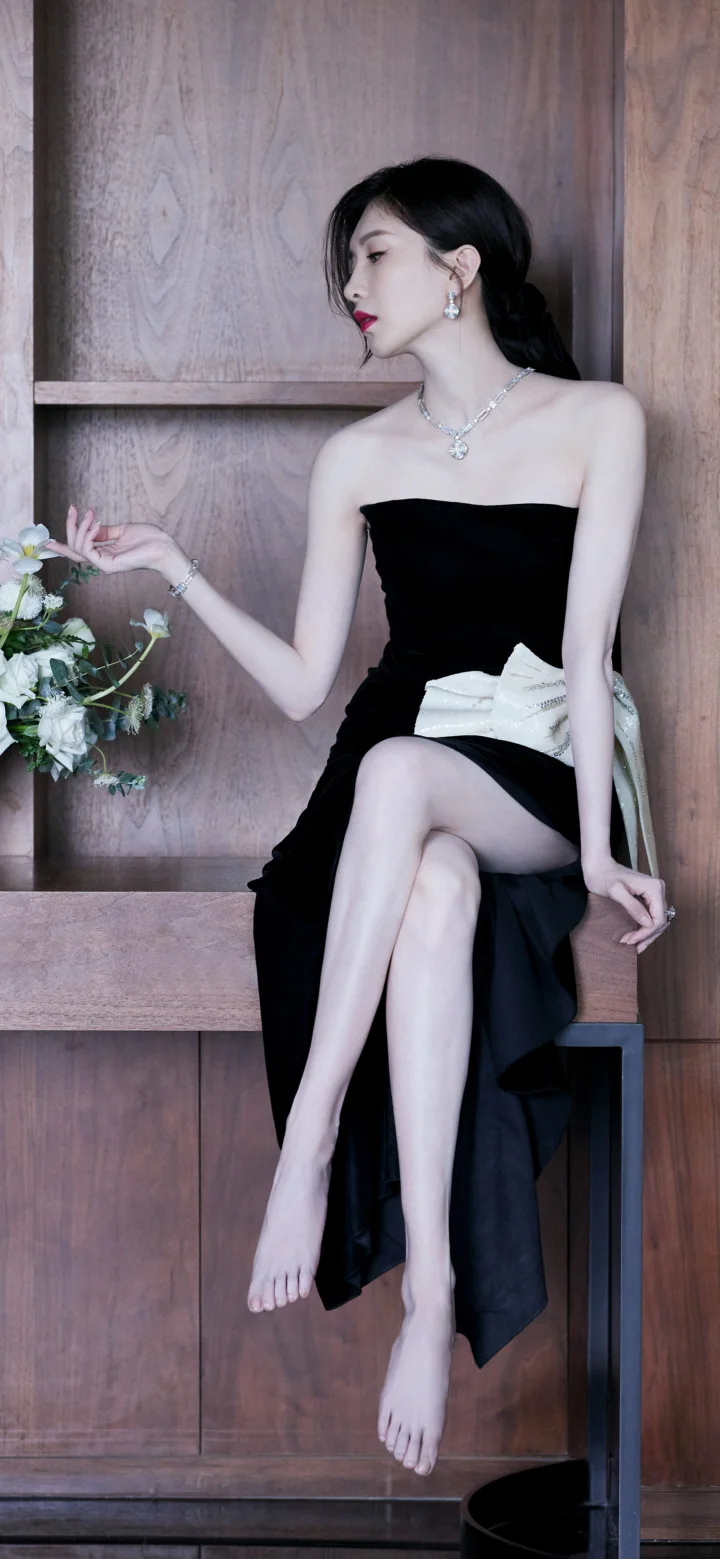 검은색 끈 없는 드레스를 입은 여성이 꽃 장식 옆 나무 배경에 앉아 있습니다.