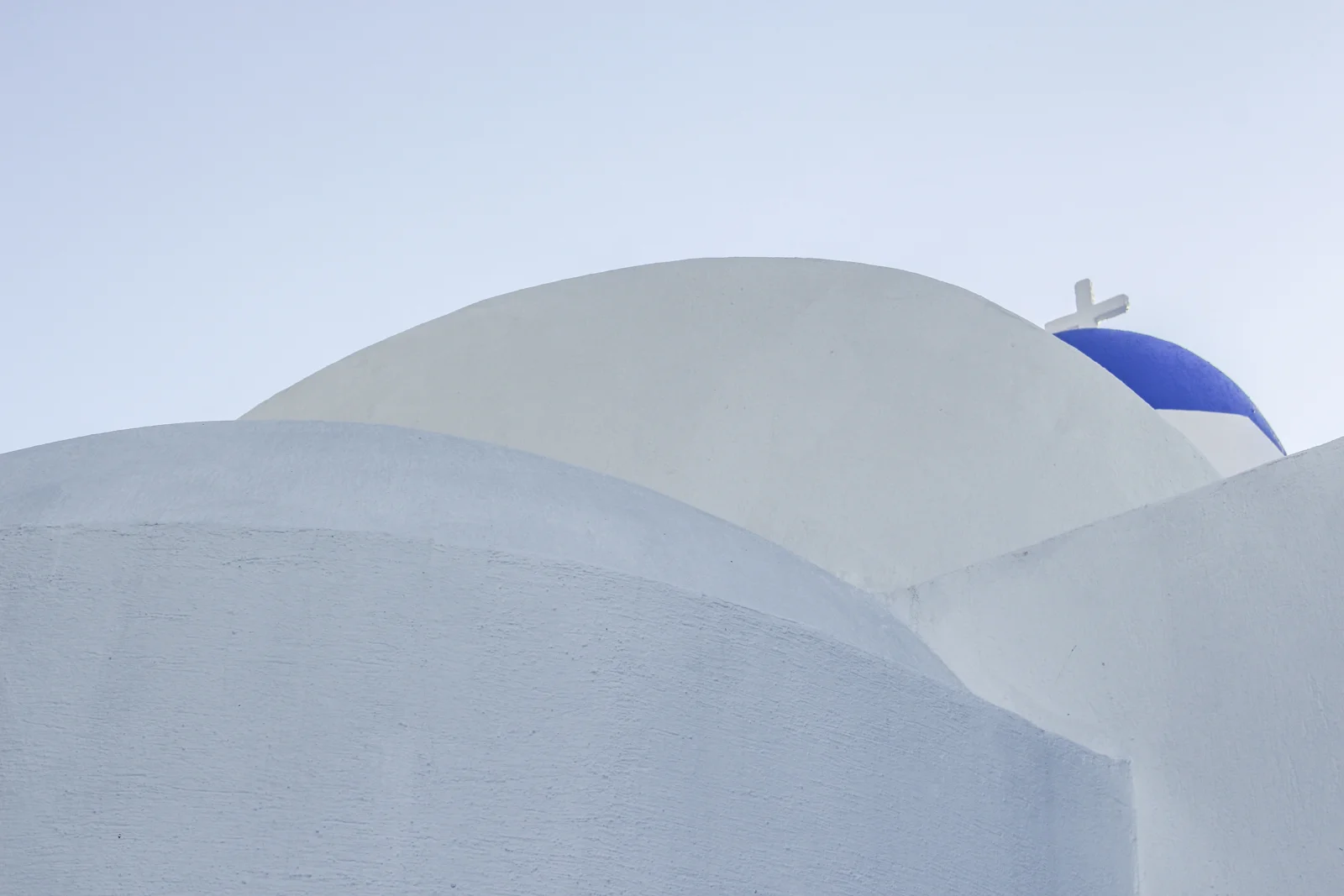 画面展示了蓝天下层叠的白色建筑曲面和一座蓝顶圆顶。