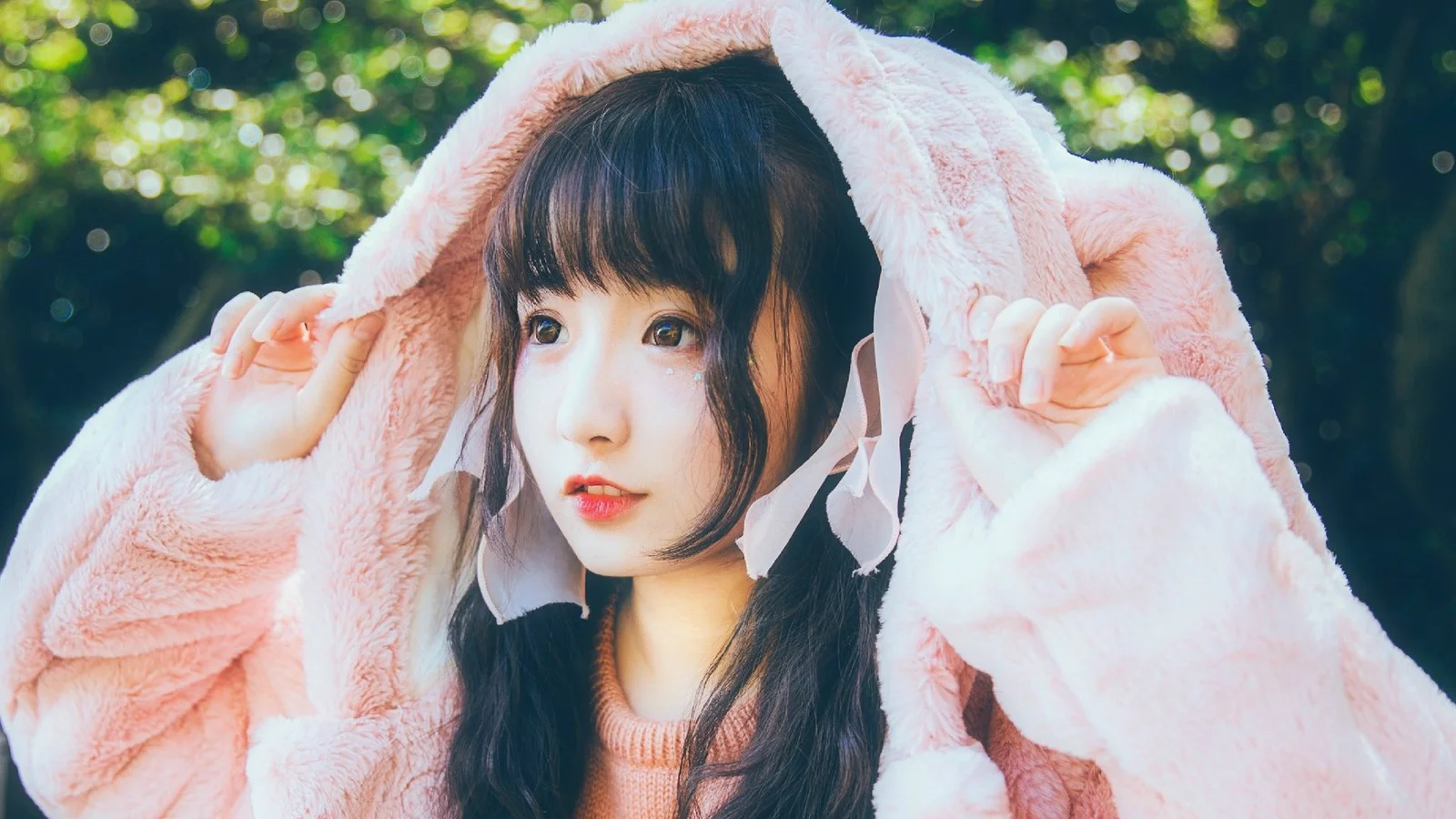 屋外でピンクのふわふわしたフード付きジャケットを着た女性。
