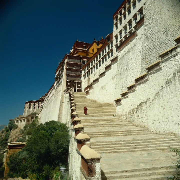 蓝天下的白色古建筑沿山坡延伸，宽阔石阶通向层叠的屋檐与墙体。