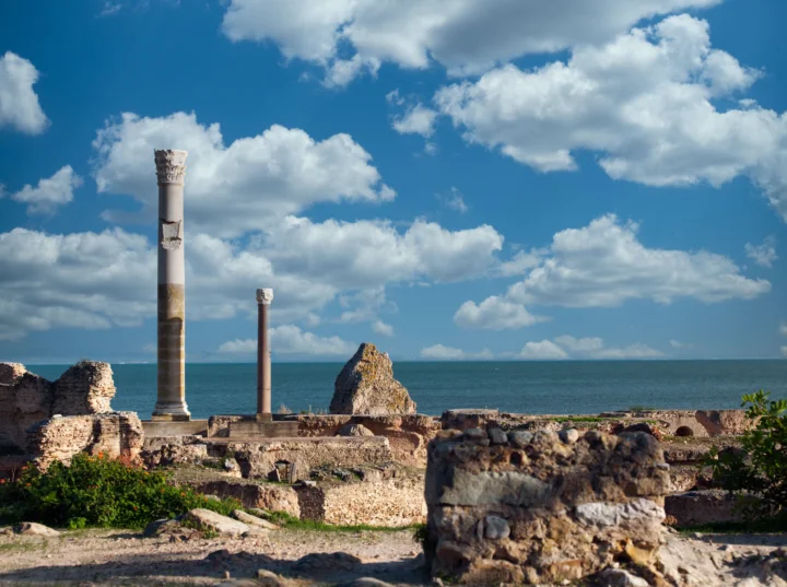 海边的古代遗迹、石柱和残墙映衬着蓝色海面与白云。