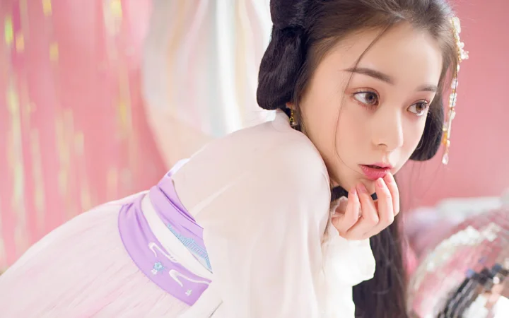 一位身穿浅色传统风格服饰的女性在粉色背景前侧身回望。