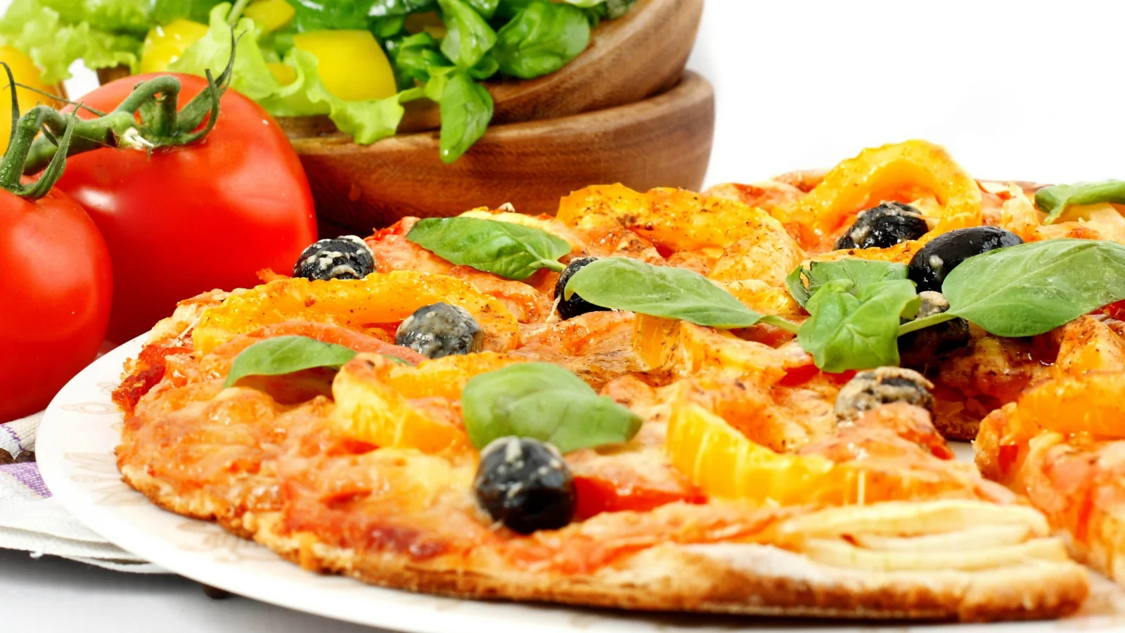 토마토, 바질 잎, 블랙 올리브를 올린 피자와 신선한 토마토, 채소 샐러드가 보입니다.
