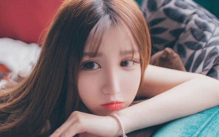 一名长发女性近距离趴在室内软垫上看向镜头。