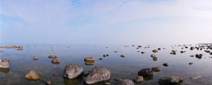 平静的海水延伸至远方，前景散布着大小不一的岩石，天空明亮开阔。