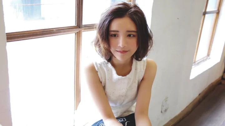 一位短发女性坐在明亮窗边，面向镜头微笑。