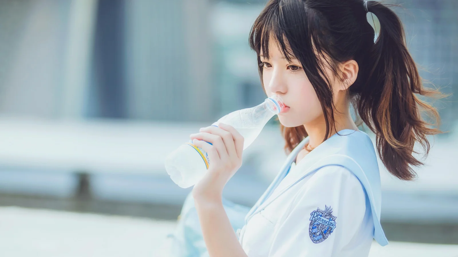 一名扎着马尾的年轻女性在户外拿着水瓶饮水。