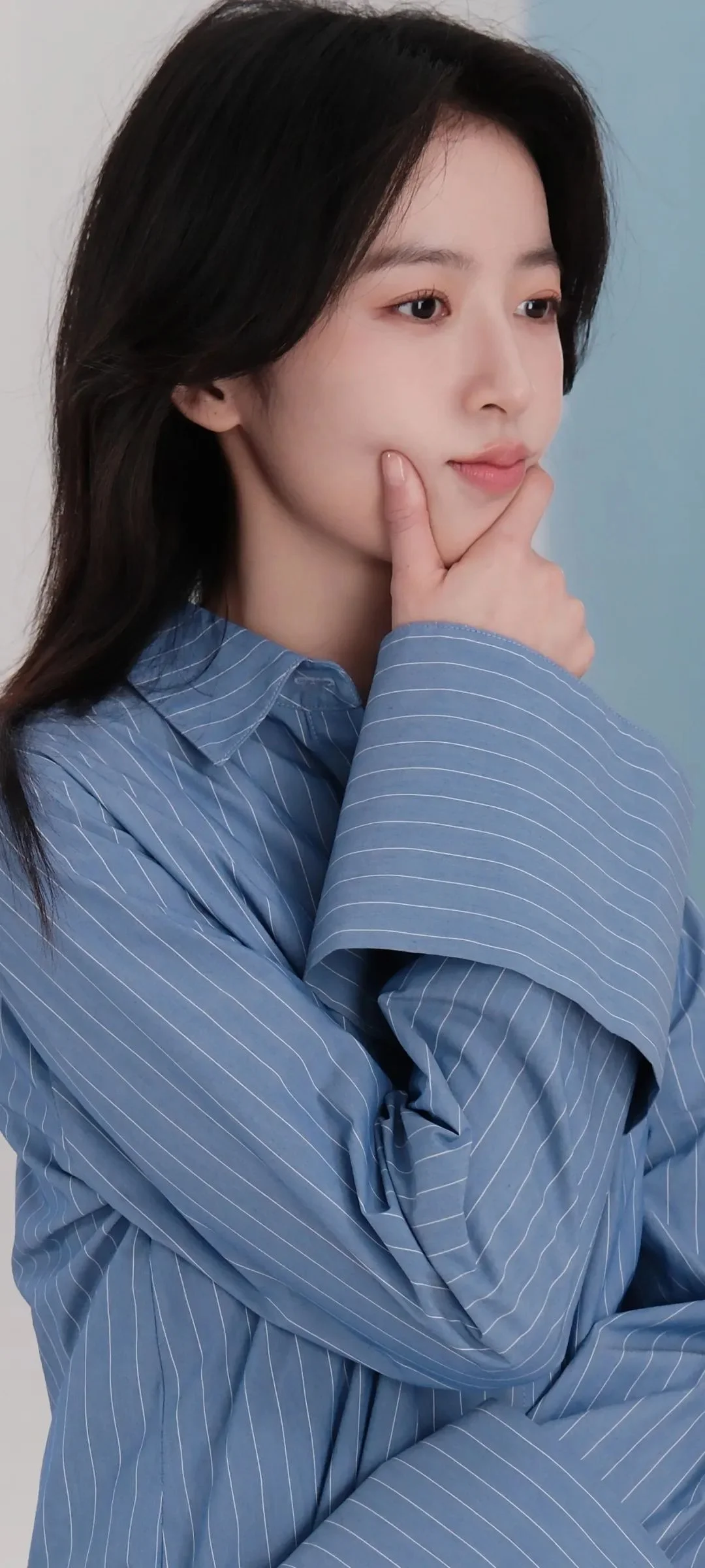 一名女子身穿蓝色条纹衫，用手托着下巴，背景为浅蓝灰色。