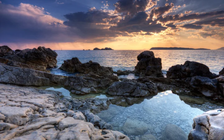夕阳映照着海面、岩石海岸和潮池，天空布满绚丽的云层。