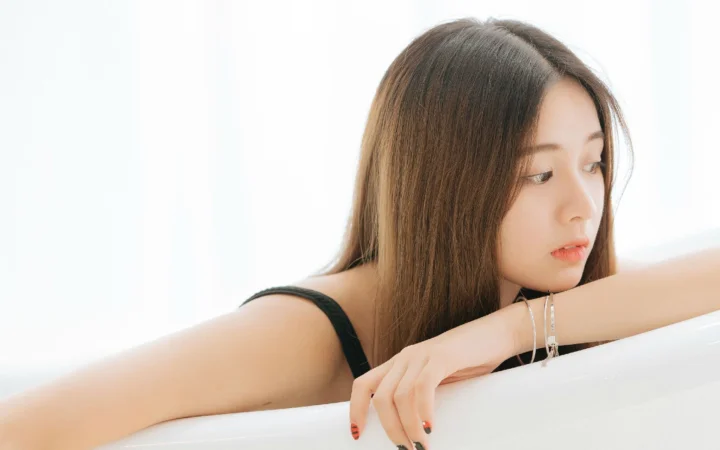 一位棕色长发女性靠在白色表面上，侧头望向右侧。