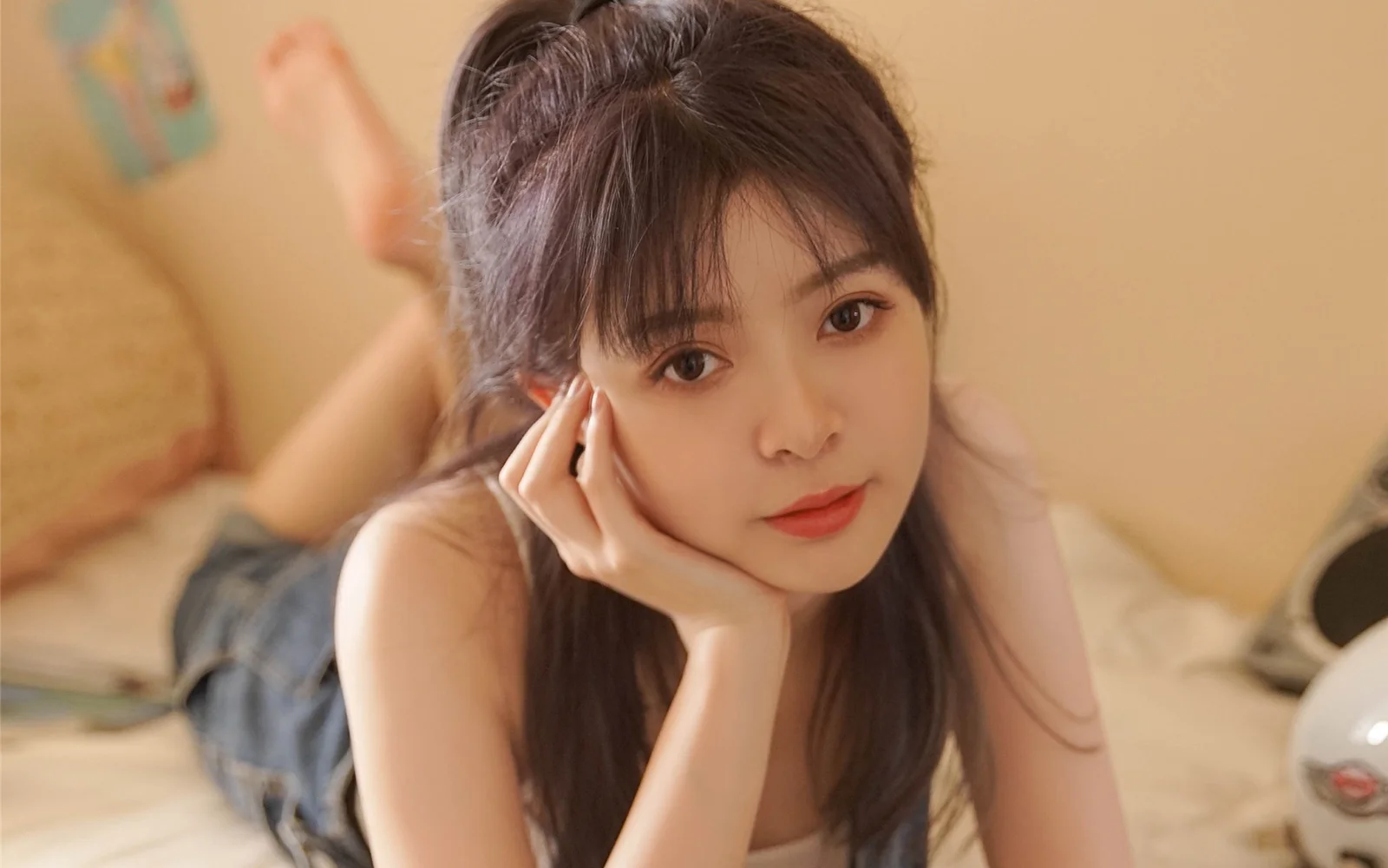 一名长发女性躺在床上，用双手托着脸，在温暖的室内光线下看向镜头。