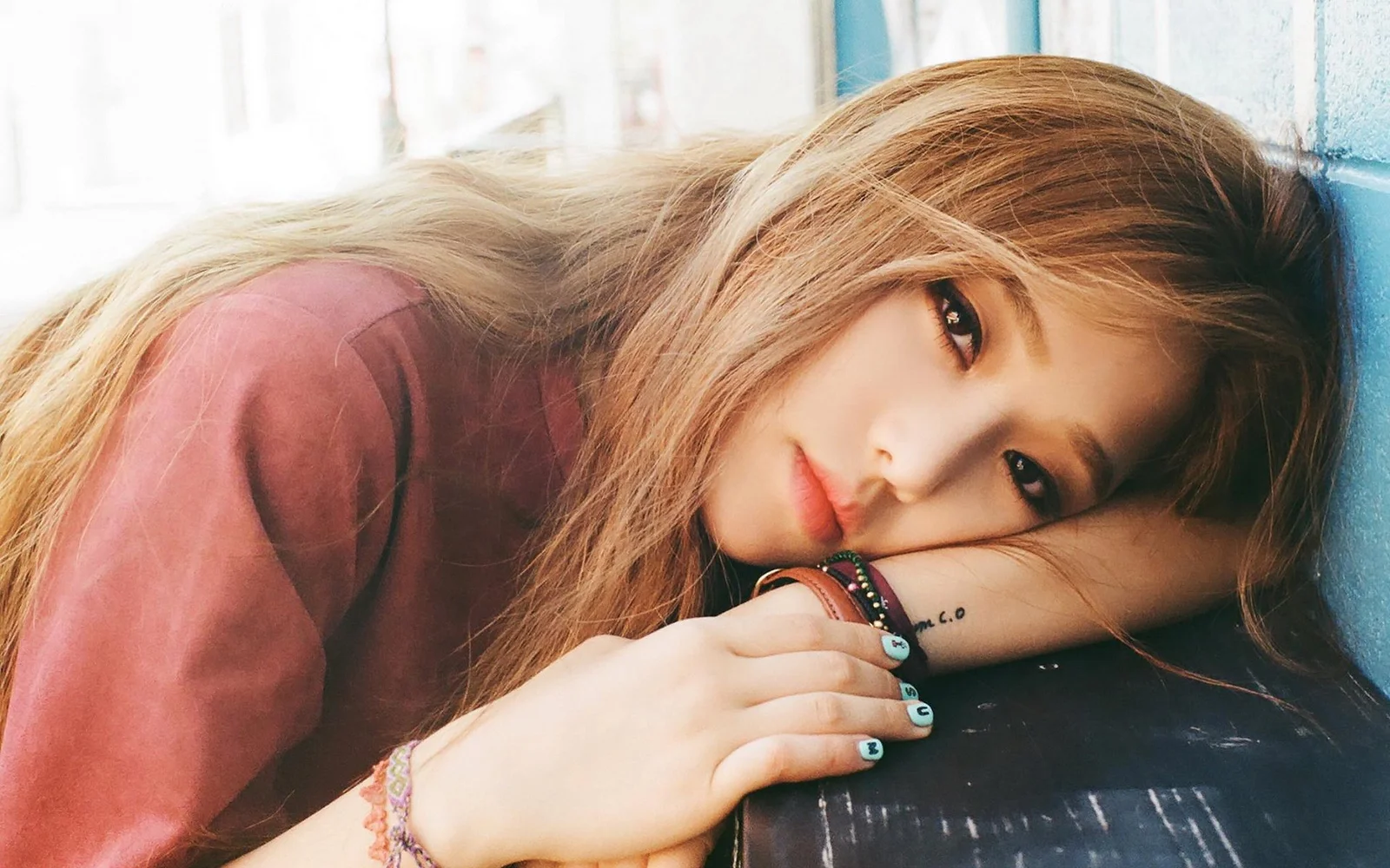 一名长发女子侧身靠在窗边，手臂支着脸颊并望向镜头。