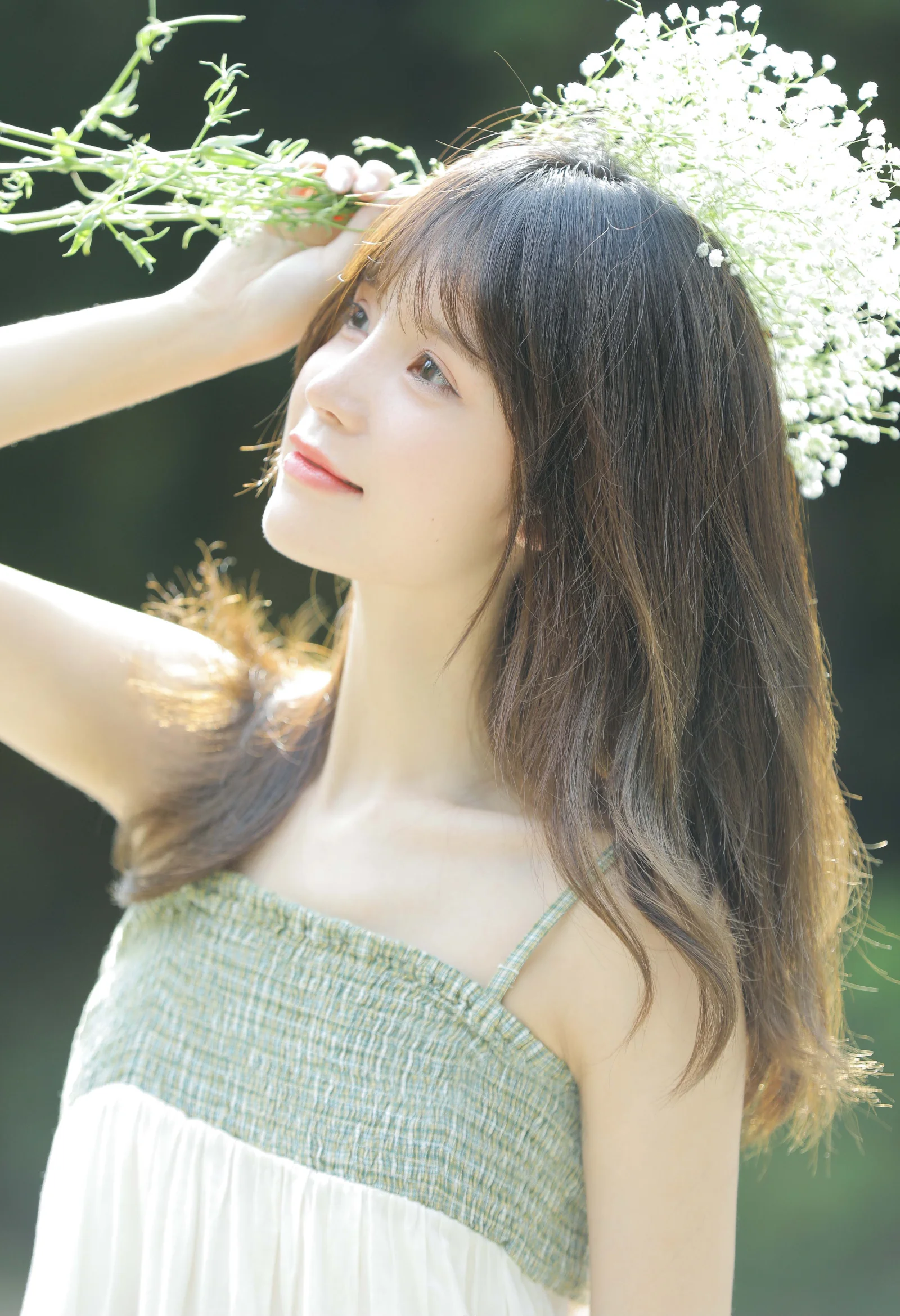 一位長髮女子在戶外白色花朵旁抬頭微笑。