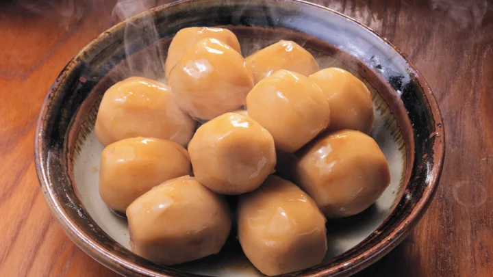 一只深色陶碗中盛着几颗表面光滑的金黄色食物，放在木桌上并冒着热气。