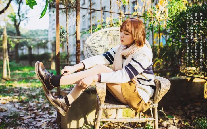성인 여성이 정원의 라탄 의자에 앉아 식물 사이로 비치는 햇살 속에서 신발끈을 정리하고 있다.