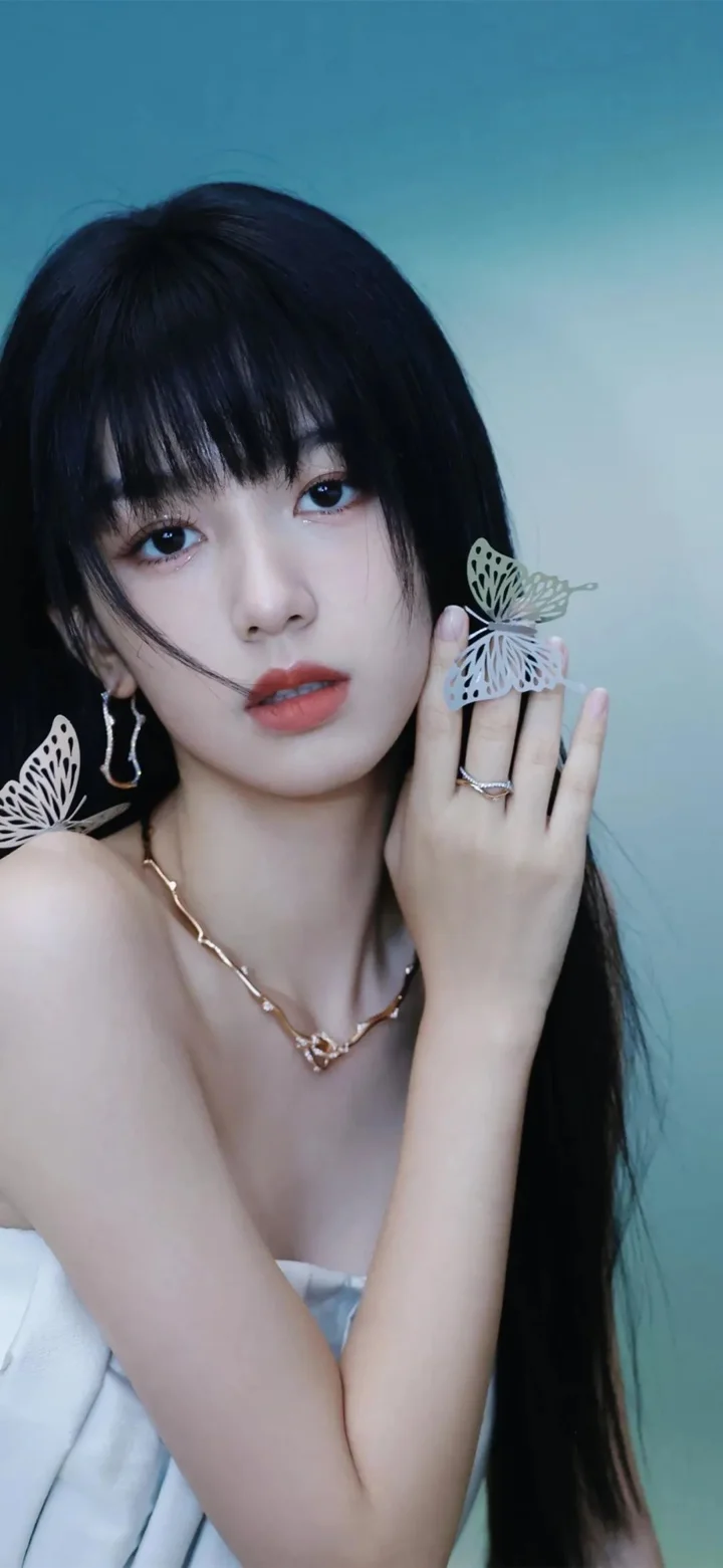 一位黑发女性手持蝴蝶装饰靠近脸颊，背景为蓝绿色调。