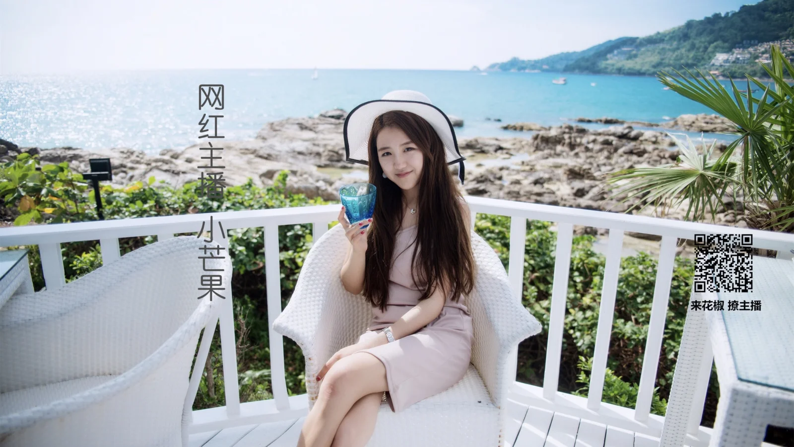 흰 모자와 분홍색 옷을 입은 여성이 파란 음료를 들고 바닷가의 흰 의자에 앉아 있습니다.