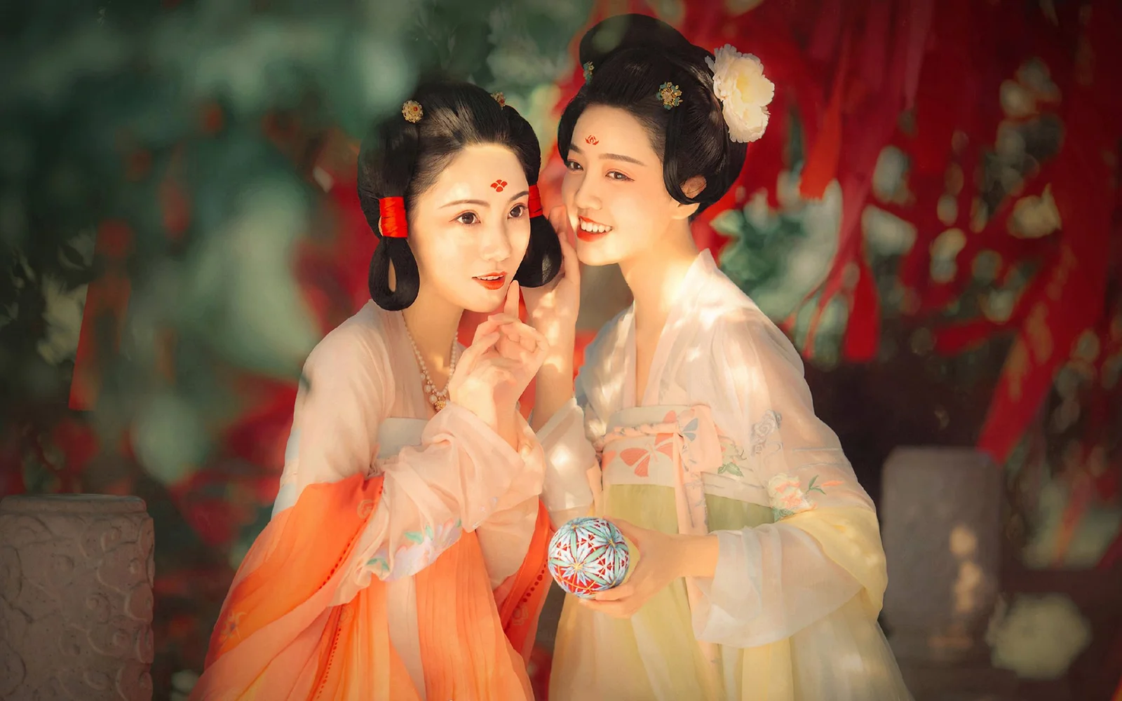 两位身穿传统服饰并佩戴发饰的女性在红绿装饰背景前合影。