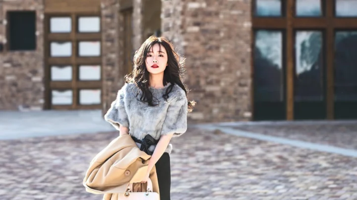 한 여성이 벽돌 건물 앞 야외 포장 공간에 서 있습니다.