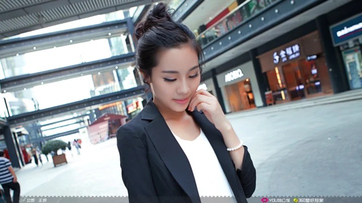 一名身穿黑色西装外套的成年女性站在现代商场中。