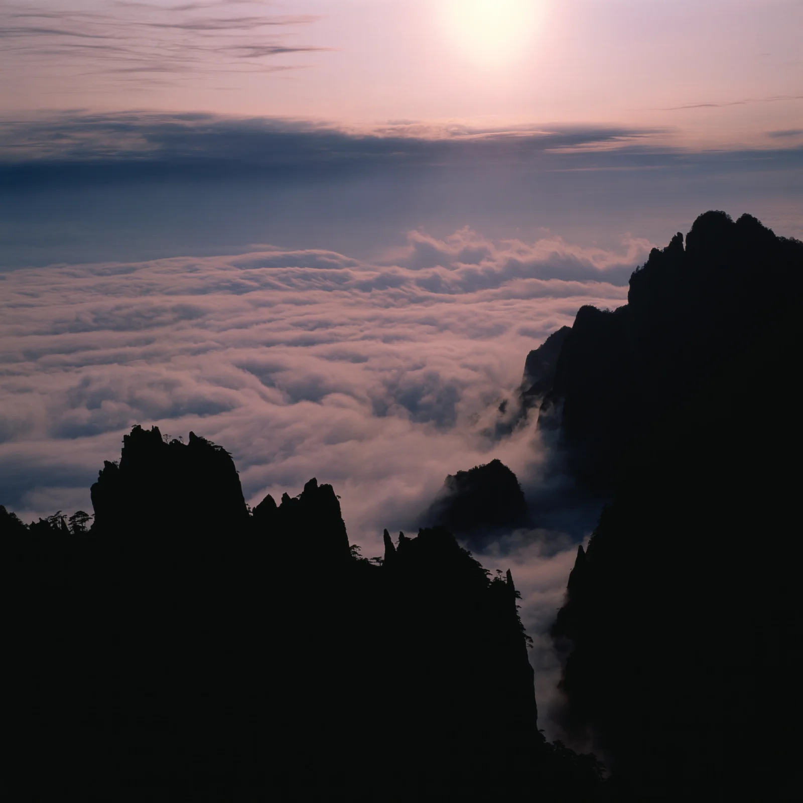 暮色天空下，深色山峰环绕着翻涌的云海。